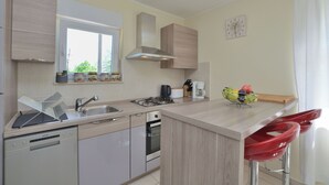 Een moderne keuken met een vaatwasser, fornuis en spoelbak. Op het aanrecht staan twee rode barkrukken en een fruitschaal.