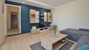 Een moderne woonkamer met een flatscreen televisie, houten kasten, een grijze bank en een salontafel.