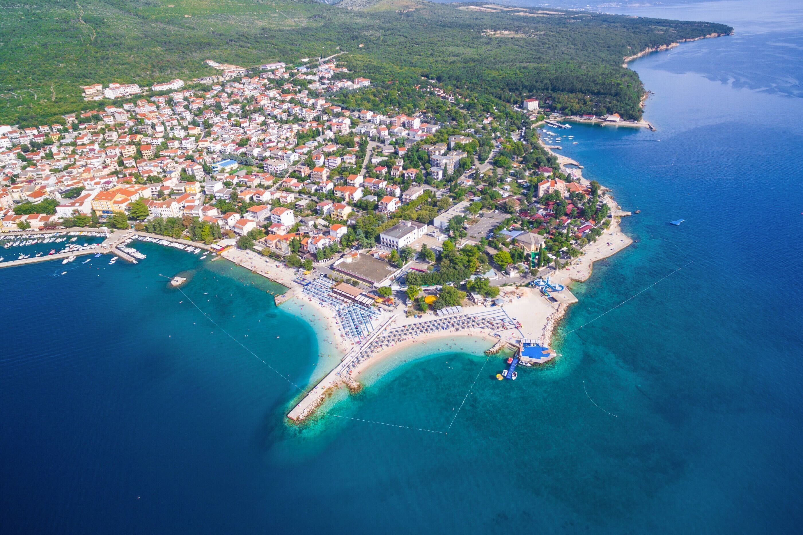 Vue aérienne d’une ville côtière avec un port de plaisance, des plages de sable et des quartiers résidentiels densément peuplés.