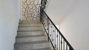 Una escalera con escalones de madera y barandilla de metal negro que lleva a una habitación con pared de piedra.