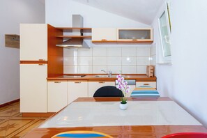 A modern kitchen with wooden cabinets, a stainless steel sink, and a vase with flowers on the table. - Apartments Dream View (Brela)