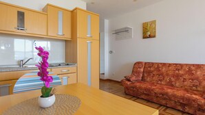 A modern kitchen with wooden cabinets, a dining table with a vase of purple flowers, and a patterned sofa in a living area. - Apartments Dream View (Brela)