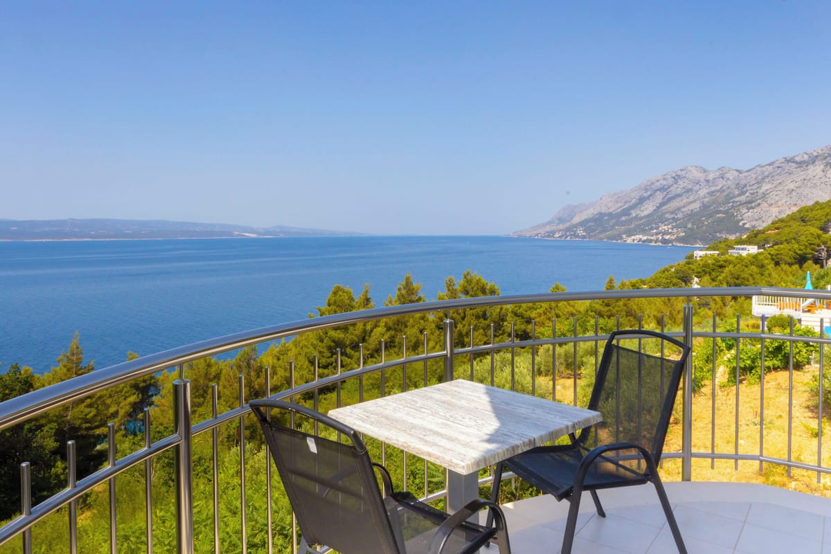 A balcony with a table and chairs overlooking a body of water and a mountainous landscape.