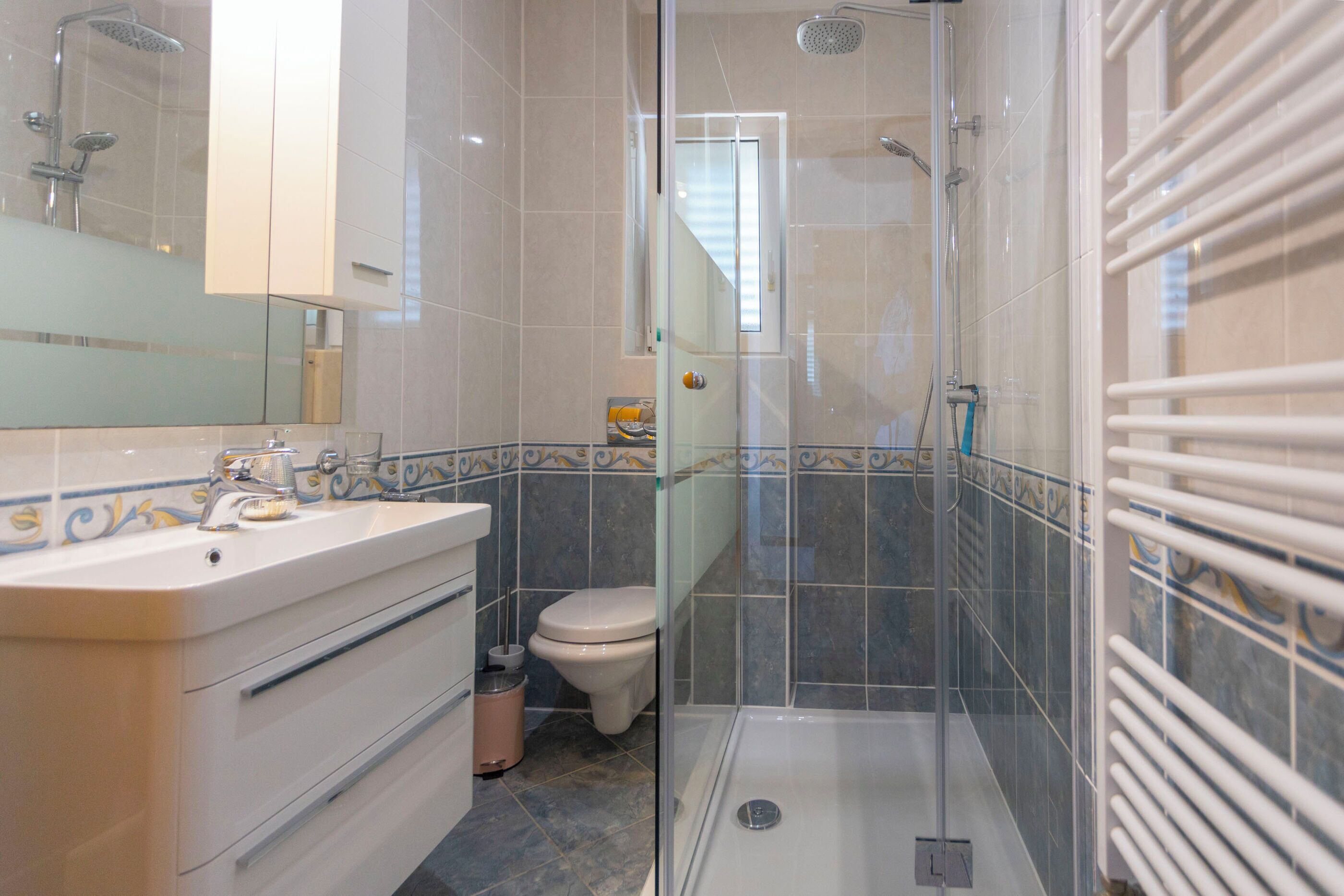 Uma casa de banho moderna com chuveiro envidraçado, lavatório branco com espelho e sanita.