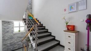 A staircase with a metal railing, a white cabinet with drawers, and a window with a plant. - Apartments Dream View (Brela)