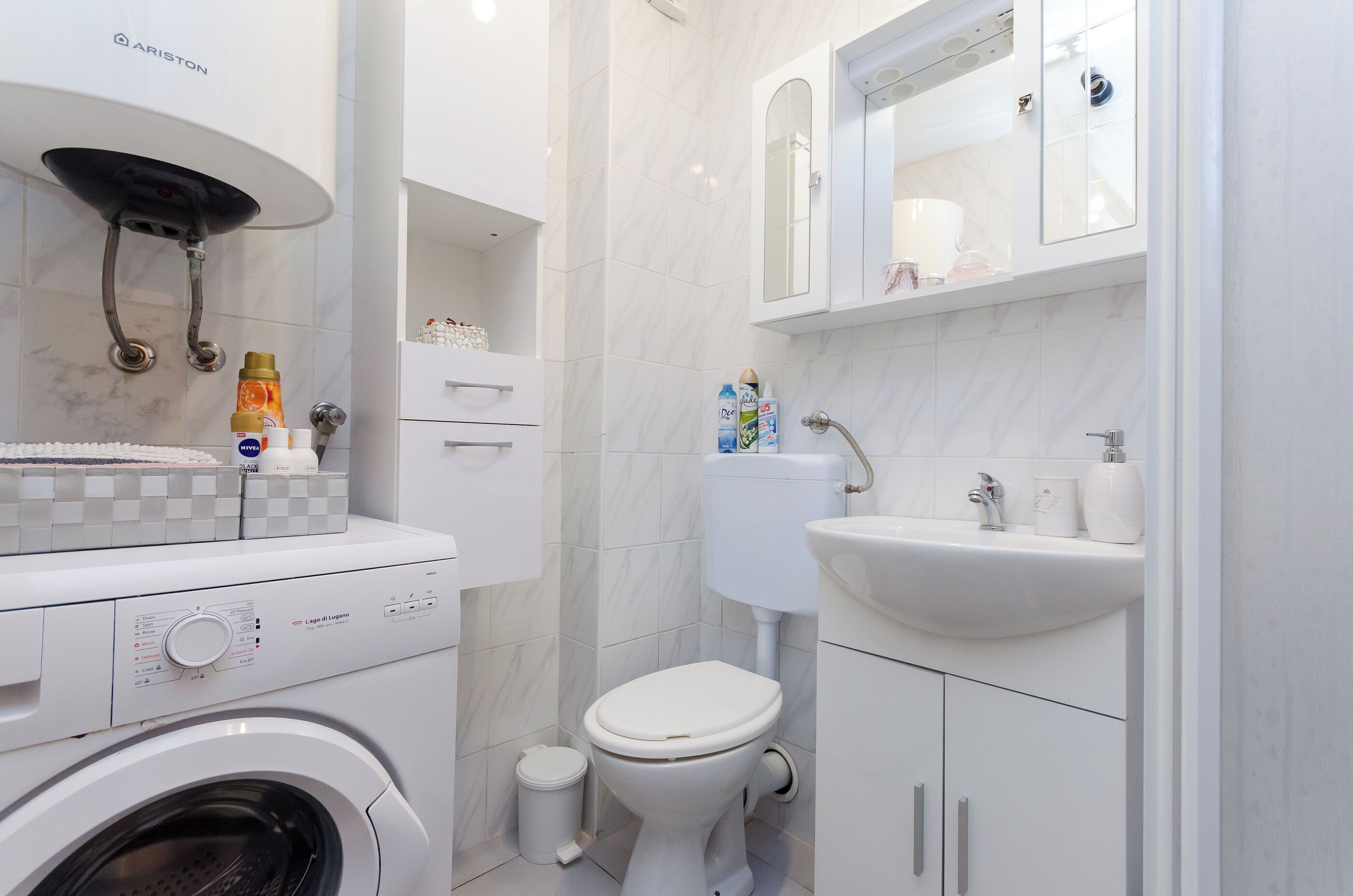 A modern bathroom with a washing machine, toilet, sink, and a mirror above the sink.
