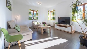 Een moderne woonkamer met een bank, een groene fauteuil, een salontafel, een televisie en een kamerplant.