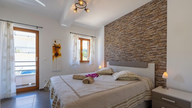 Een slaapkamer met een groot bed, een nachtkastje, een wandlamp en een raam met gordijnen.