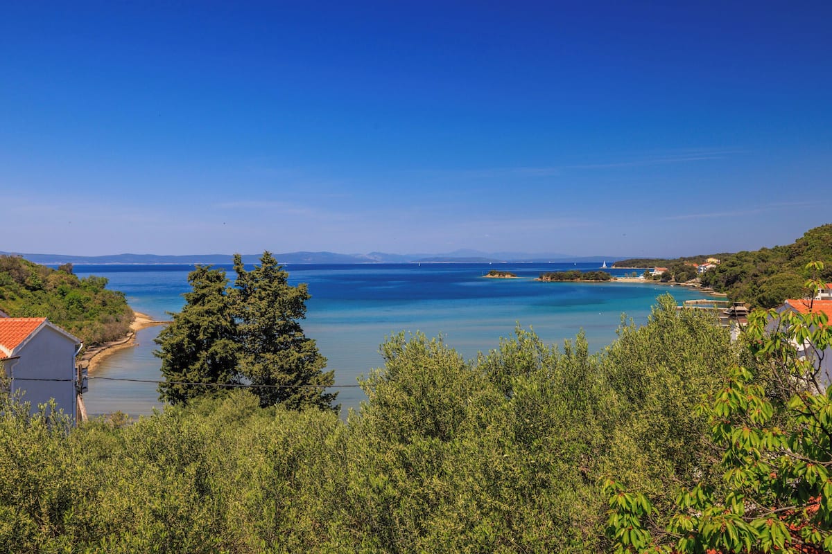 Un paysage côtier offrant une vue dégagée sur la mer, avec quelques bâtiments et une végétation luxuriante.