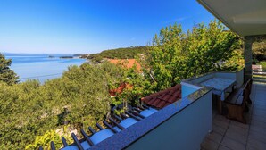 A balcony with a view of the sea, surrounded by greenery and a tiled floor. - Apartments Marija G (Rab)