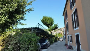 A narrow street with parked cars, a pedestrian bridge, and buildings with shutters. - Apartments Lory (Labin)