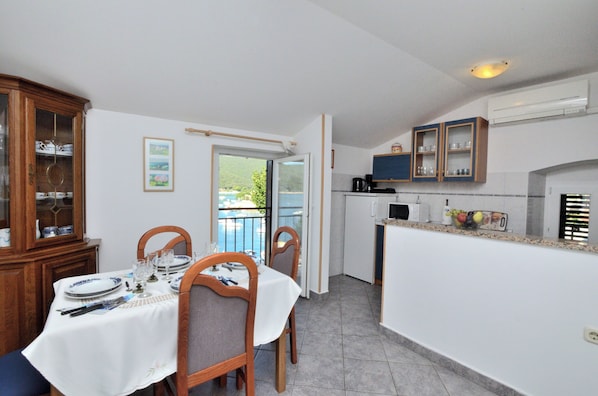 A dining area with a table set for four, a kitchen with cabinets and appliances, and a view of greenery outside. - Apartments Lory (Labin)