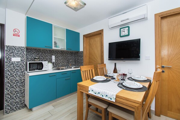 A modern kitchen with teal cabinets, a microwave, and a dining table set for two. - Apartment Lucija (Vodice)