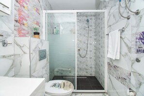 A modern bathroom with a glass-enclosed shower, marble tiles, and a toilet with a decorative stone design. - Apartment Lucija (Vodice)