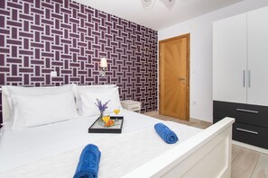 A hotel room with a patterned wall, a bed with white linens, a tray with breakfast, and a wooden door. - Apartment Lucija (Vodice)