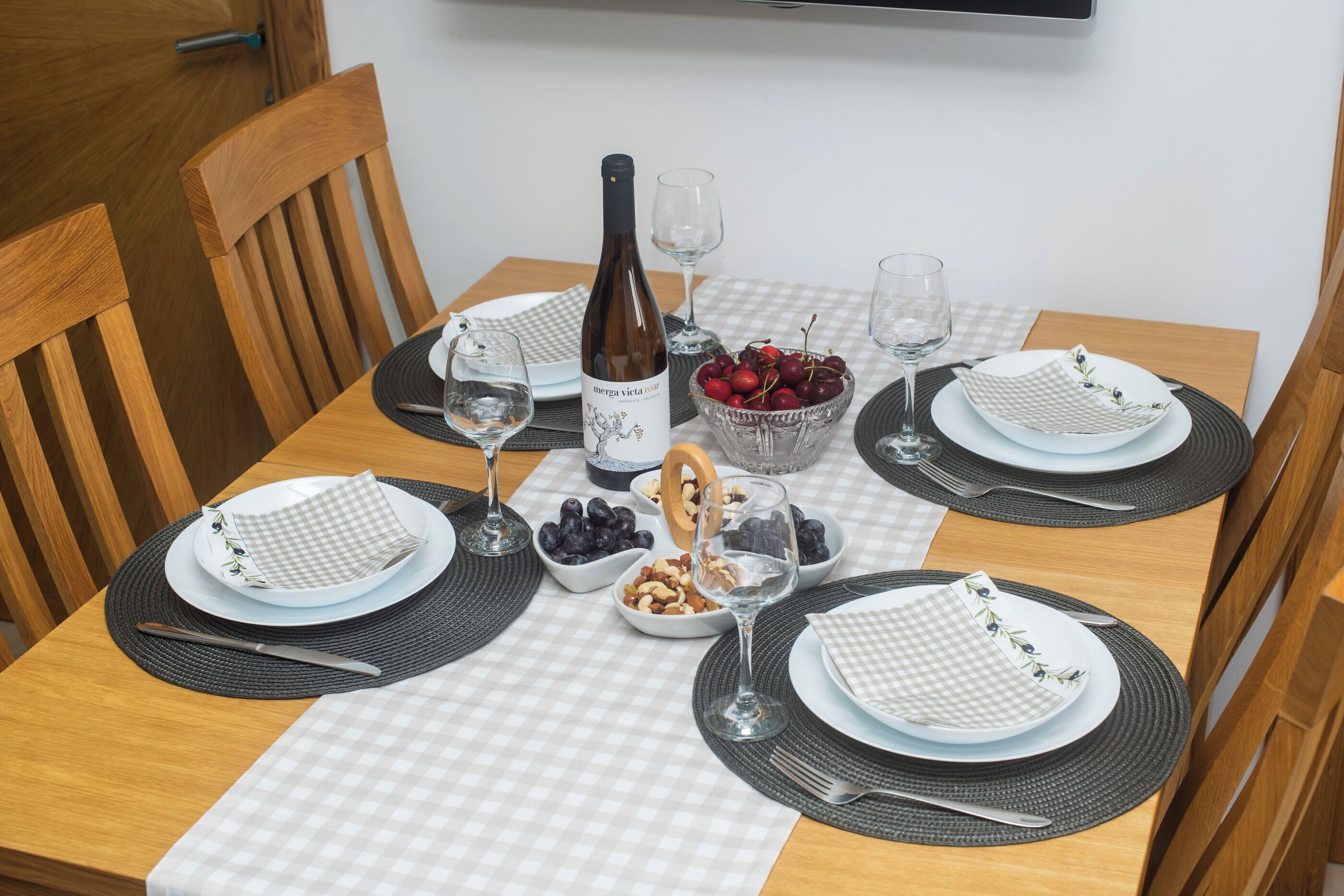 Uma mesa de jantar posta com pratos, talheres, uma garrafa de vinho e tigelas de frutas e nozes.