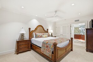 A bedroom with a wooden bed, two bedside tables with lamps, a ceiling fan, and a bathroom visible through an open door. - Stunning Beachfront Condo at Makena Surf Resort #E104 with Panoramic Ocean Views (Makena, Maui)