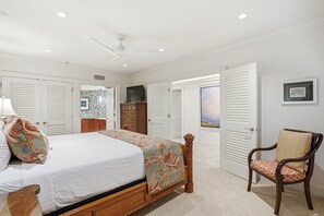 A bedroom with a bed, a chair, a wardrobe, and a television. - Stunning Beachfront Condo at Makena Surf Resort #E104 with Panoramic Ocean Views (Makena, Maui)