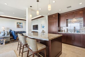 A modern kitchen with dark wood cabinets, a marble countertop, and a bar area with stools. - Stunning Beachfront Condo at Makena Surf Resort #E104 with Panoramic Ocean Views (Makena, Maui)