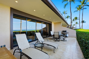 A modern outdoor patio with lounge chairs, a table, and a grill area. - Stunning Beachfront Condo at Makena Surf Resort #E104 with Panoramic Ocean Views (Makena, Maui)