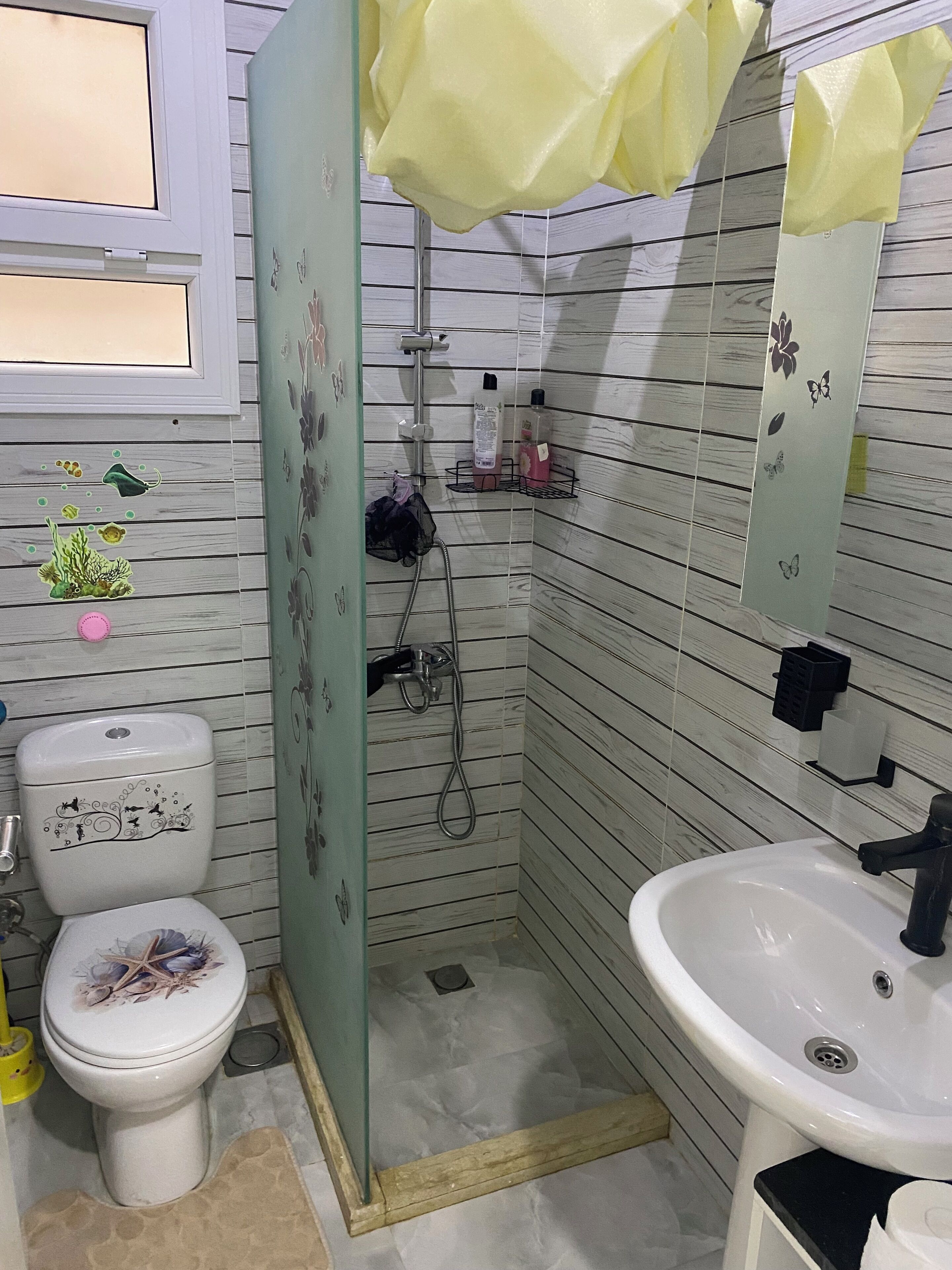 A bathroom with a toilet, sink, shower, and decorative elements on the walls.