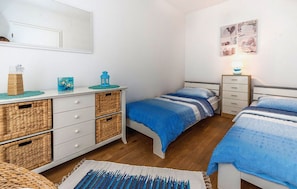 Ein Schlafzimmer mit zwei Betten, einem Schminktisch, Korbwannen, einer Wanddekoration und einer Nachttischlampe.