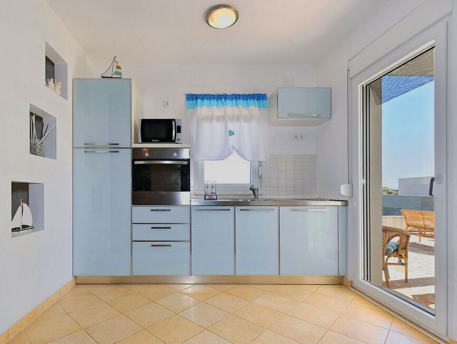 Cucina compatta con microonde, forno e lavello, caratterizzata da mobili azzurri e vista all'esterno.