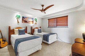 Ein Schlafzimmer mit zwei Betten, einem Deckenventilator, einer Gitarre und einem Fenster mit Jalousien.