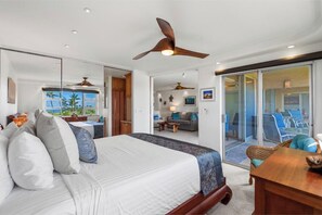 A bedroom with a bed, ceiling fans, a view through a sliding door to a balcony, and a dining area. - Renovated 2BR w/ AC - Menehune Shores #522 Oceanview South Maui Condo Getaway (Kihei, Maui)