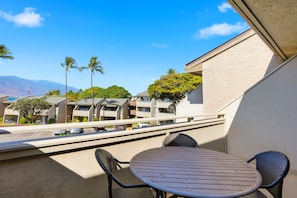 A balcony with a round table and two chairs, overlooking a parking area and buildings with a mountain in the background. - Beautifully Remodeled 2 Bedroom/ 2 Bath- Stunning Views - Kihei Holiday #315 (Kihei, Maui)