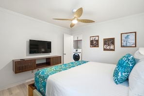 A bedroom with a bed, a ceiling fan, a television, a washing machine, and framed pictures on the wall. - Beautifully Remodeled 2 Bedroom/ 2 Bath- Stunning Views - Kihei Holiday #315 (Kihei, Maui)