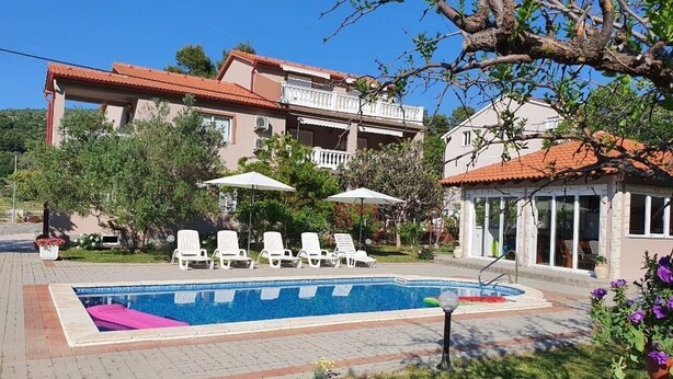 Un edificio a due piani con piscina, lettini e ombrelloni.