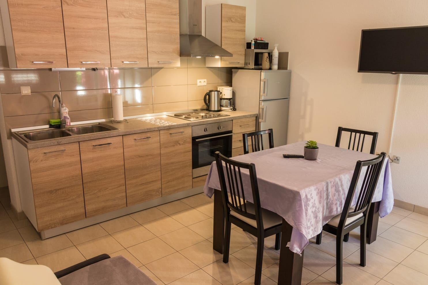 A modern kitchen with wooden cabinets, a stainless steel sink, and a dining area with a table and chairs.