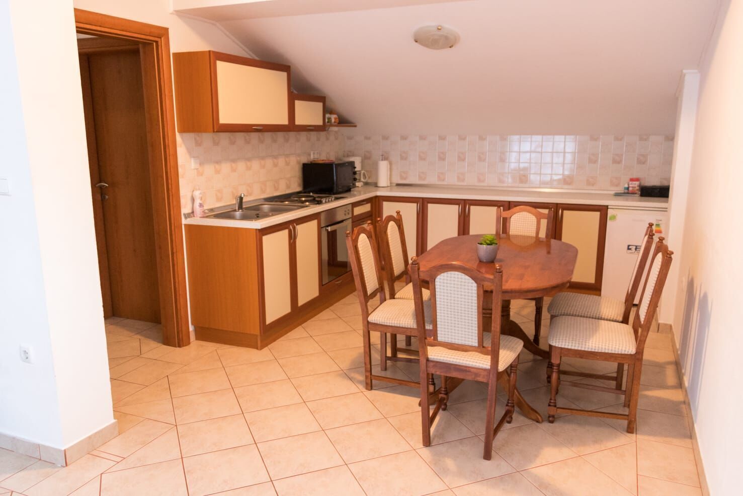 Una cucina compatta con mobili in legno, un tavolo da pranzo con sedie e un'isola piccola.
