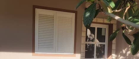 A patio with a wooden table and benches, a door, and a window with shutters.