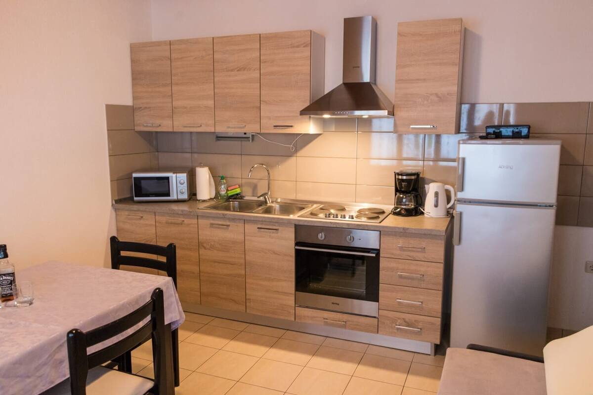 A compact kitchen with wooden cabinets, a stainless steel range hood, a microwave, a coffee maker, and a refrigerator.