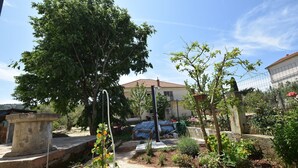 A garden with a stone bench, a tree, and a building in the background. - House Periska (Pasman)