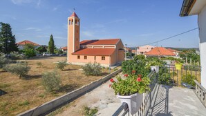 A residential area with a church featuring a bell tower, a paved pathway, and potted plants on a balcony. - House Periska (Pasman)