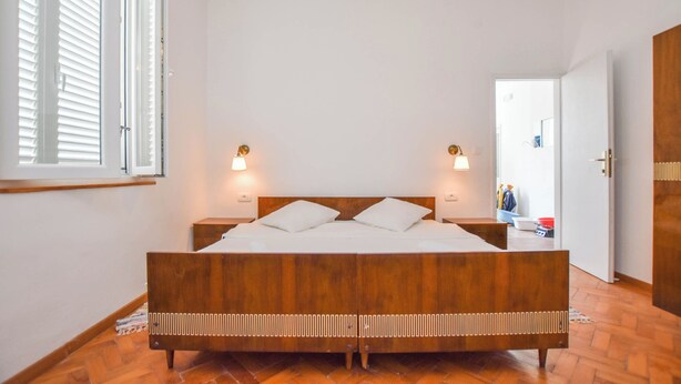 A bedroom with a wooden bed, two bedside lamps, and a view of a hallway with a door. - House Periska (Pasman)