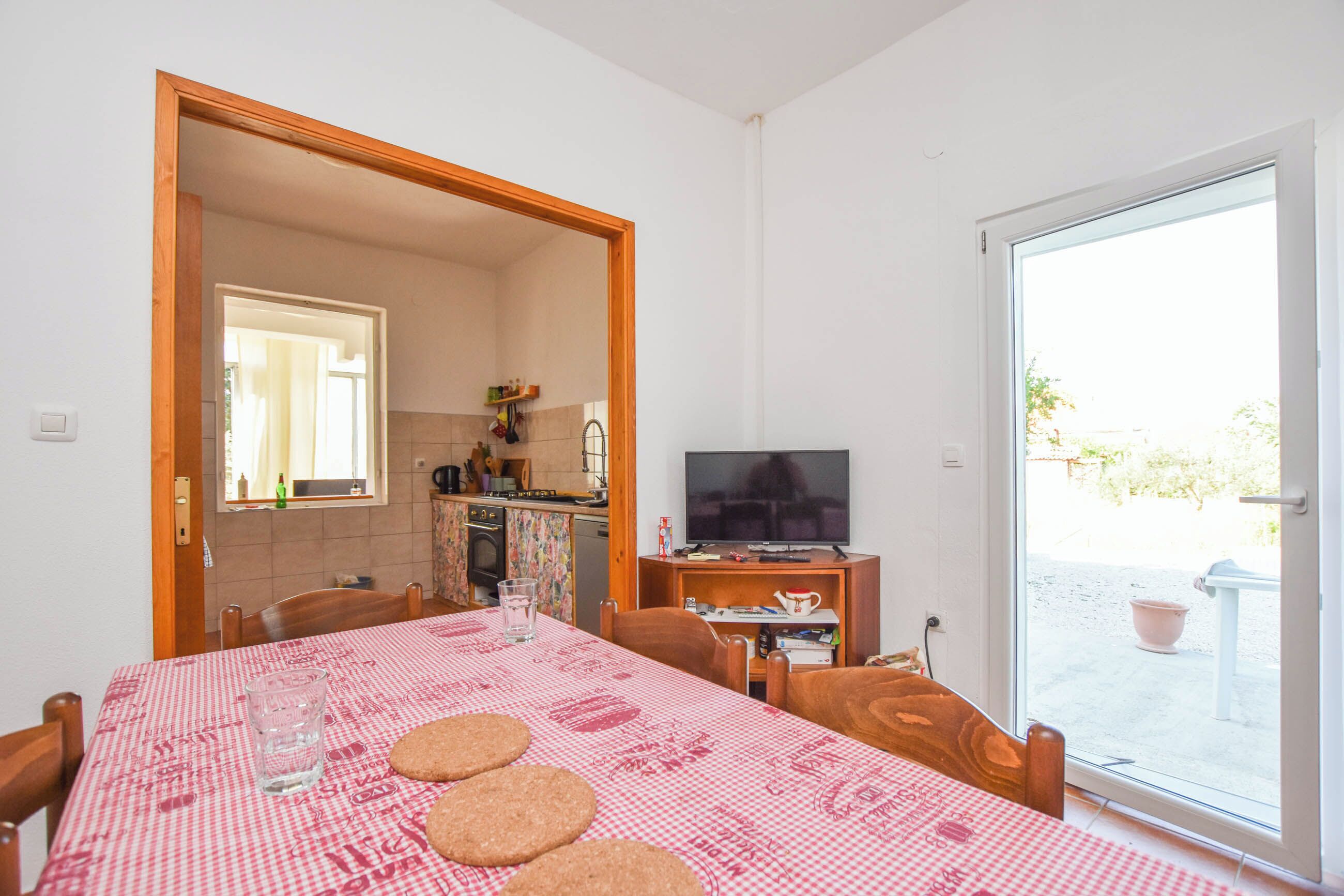 Un coin repas avec une table dressée pour quatre personnes, un téléviseur posé sur un meuble et une vue sur l’extérieur grâce à une porte vitrée.