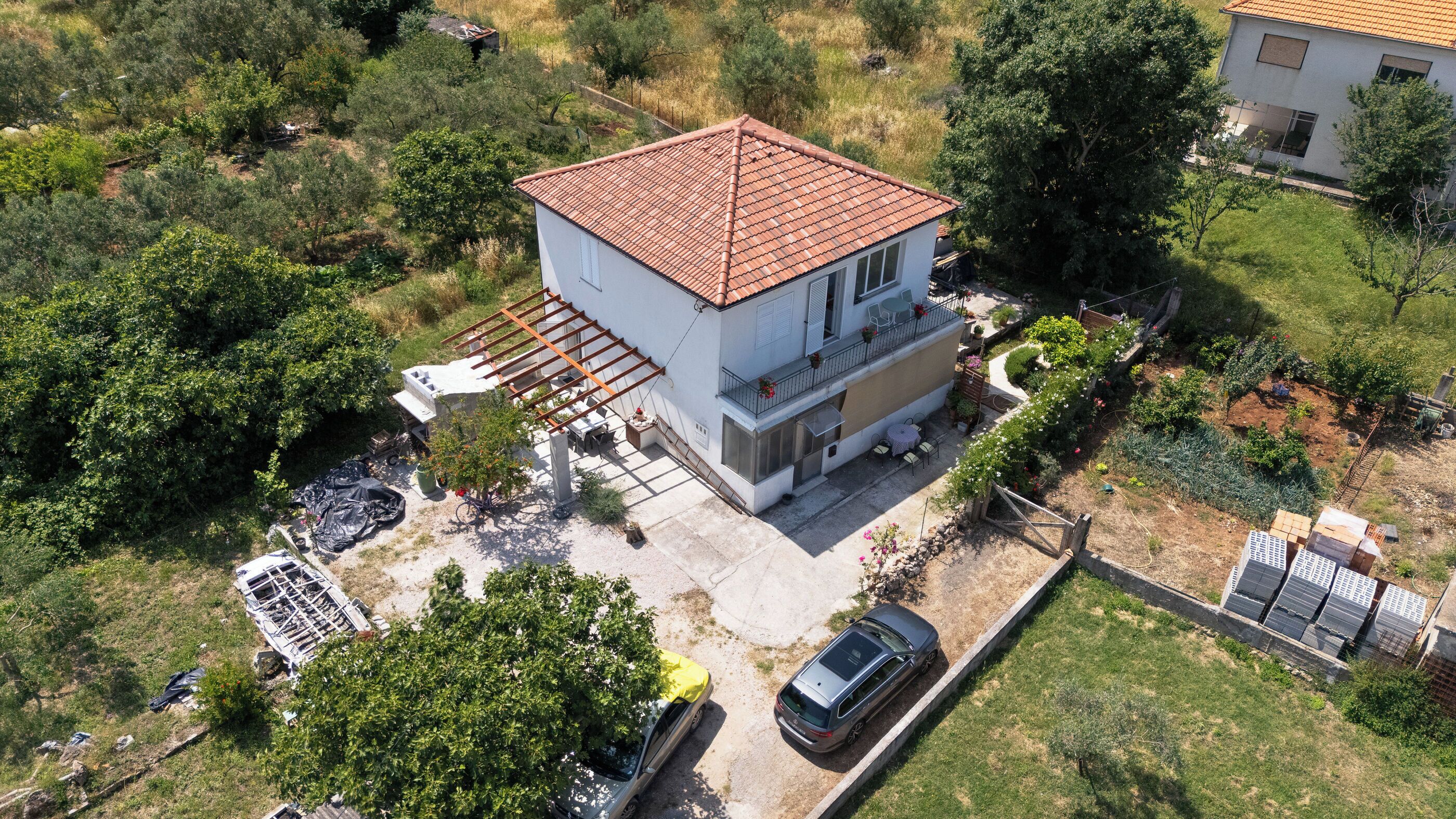 A two-story house with a tiled roof, surrounded by greenery and a garden.