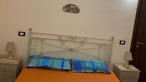 Ein Schlafzimmer mit einem Bett, zwei Nachttischen, einer Wandleuchte, einem dekorativen Element und einem kleinen Fenster.