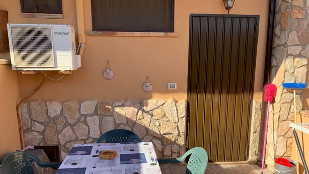 Eine Terrasse im Freien mit Tisch, der mit einer Tischdecke bedeckt ist, Steinmauern, einem Metallgitter und Reinigungswerkzeugen.