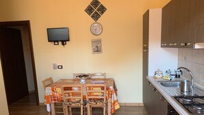 Eine kleine Küche mit Essbereich, einem an der Wand montierten Fernseher und einer Uhr.