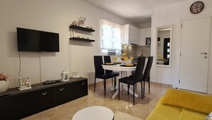 A modern living room with a flat-screen TV, a dining area with a table and chairs, a yellow sofa, and a kitchen in the background. - House Relaxing Oasis (Stari Grad)