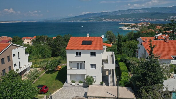 Un edificio residenziale con tetto in tegole rosse, un'antenna parabolica e vista sul mare e sulle montagne sullo sfondo.