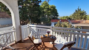 A balcony with a white railing, a small table with a vase of flowers, and a chair. - Apartment Close to the Beach (Stari Grad)