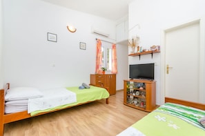 A bedroom with a bed, a TV stand with a TV, a wardrobe, and a shelf with decorative items. - Apartment Close to the Beach (Stari Grad)