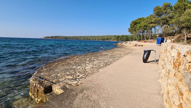A coastal walkway with a stone wall on one side and a clear blue sea on the other. - Apartment Close to the Beach (Stari Grad)
