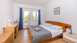 A bedroom with a bed, bedside table, desk, and a window with curtains. - Apartment Close to the Beach (Stari Grad)
